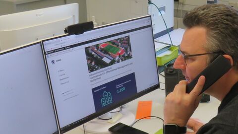 männliche Person die am Computer liest und dabei telefoniert