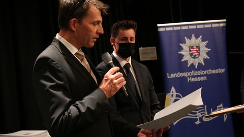 Graduierung 2022 Herr Neumeyer übergibt Ernnenungsurkunden während der Dezentralen Graduierungsfeier am Campus Wiesbaden im Saalbau Frankfurt, im Hintergrund Rollup des Landespolizeiorchester Hessen
