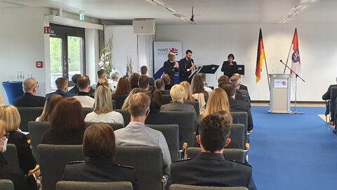 Landespolizeiorchester Hessen Drei Beschäftigte des Landespolizeiorchester Hessen mit Blasinstrumenten spielen anlässlich der Gründungsfeier der HöMS am 16. September 2022, daneben Rednerpult und im Hintergrund Deutschlandfahne und Hessenfahne