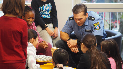 Polizeipatenprogramm: Pilotprojekt zwischen der HöMS und der Jugendbücherei in Kassel gestartet Bild zeigt Polizeikommissaranwärter beim Vorlesen für Schülerinnen und Schüler