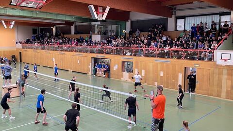 eine Sporthalle, in welcher im Vordergrund Volleyball gespielt wird, im Hintergrund viele Zuschauer auf einer Tribüne
