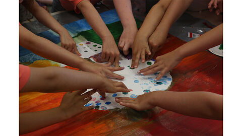 Kinderhände im Kreis um eine Leinwand herum, betupfen diese mit Fingerfarbe