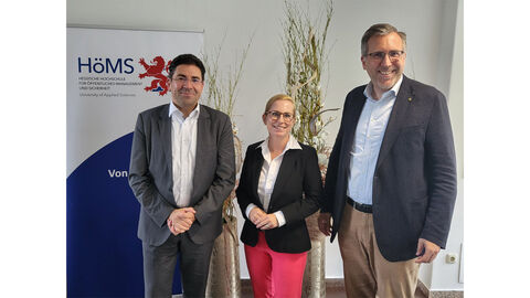 Riegerungspräsident Dr. habil. Jan Hilligardt., Dr. Seubert, Dekanin Prof. Dr. Eibelshäuser stehen vor einer Wand, im linken Hintergrund das HöMS-Logo