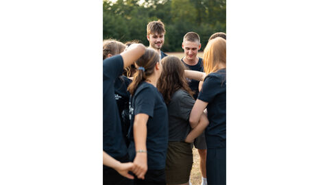 Auf dem Bild sieht man eine Gruppe von Teilnehmern des Blaulichtcamps, die auf einem Sportplatz zusammenstehen. Sie nehmen an einem Gruppenspiel teil, das darauf abzielt, die Kommunikation und das Teamwork unter den Teilnehmern zu stärken. Alle sind konzentriert und in das Spiel eingebunden, das offensichtlich darauf ausgelegt ist, das Miteinander zu fördern und die Zusammenarbeit zu verbessern. Die Stimmung wirkt lebendig und gemeinschaftlich. Auf dem Bild sieht man eine Gruppe von Teilnehmern des Blaulichtcamps, die auf einem Sportplatz zusammenstehen. Sie nehmen an einem Gruppenspiel teil, das darauf abzielt, die Kommunikation und das Teamwork unter den Teilnehmern zu stärken. Alle sind konzentriert und in das Spiel eingebunden, das offensichtlich darauf ausgelegt ist, das Miteinander zu fördern und die Zusammenarbeit zu verbessern. Die Stimmung wirkt lebendig und gemeinschaftlich.
