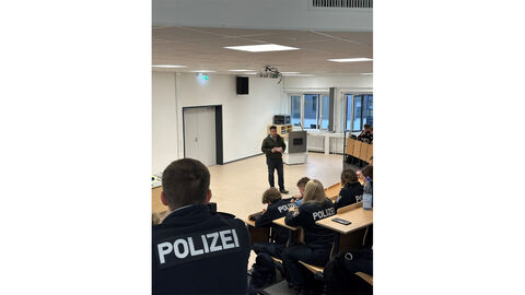 Bundestagsabgeordneter Mijatovic Blick von oberhalb in einen Hörsaal auf den Bundestagsabgeordneten Mijatovic. Dieser spricht zu Studierenden, welche im Vordergrund, auf Hörsaalbänken sitzend, zu erkennen sind und Polizeiuniformen tragen.