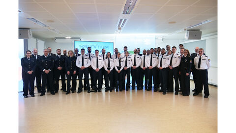 Behördenvertreterinnen und -vertreter mit Lehrgangsklasse Wachpolizei stehen vor einer Leinwand