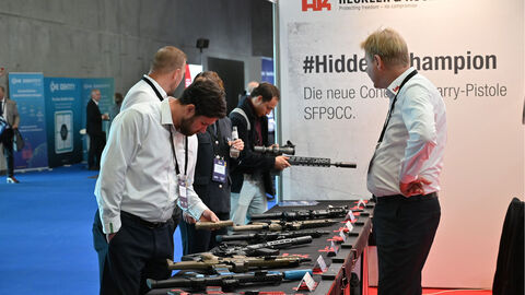 Besucher am Stand des Waffenherstellers „Heckler und Koch“. Studierender im Hintergrund hält Langwaffe in der Hand Besucher am Stand des Waffenherstellers „Heckler und Koch“. Studierender im Hintergrund hält Langwaffe in der Hand