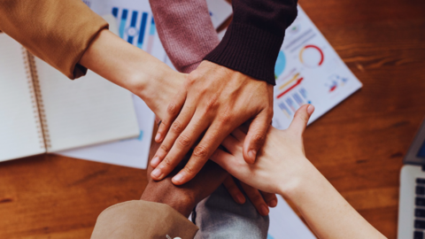Foto von sechs Händen, die übereinander gelegt sind von oben fotografiert