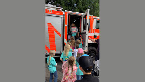 Kindergruppe am Feuerwehrwagen bei der Feuerwehr in Wiesbaden Kindergruppe steht an der offenen Tür eines Feuerwehrfahrzeugs und besichtigen den Innenraum