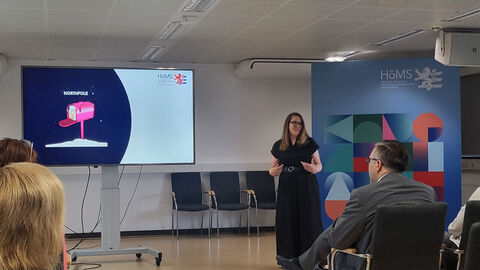 Frau steht vor Publikum und hält einen Vortrag.