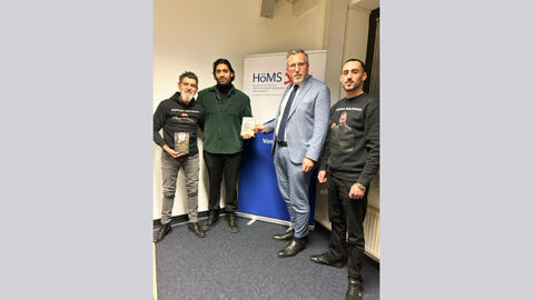 Vier Personen blicken in die Kamera, zwei halten ein Buch in der Hand.